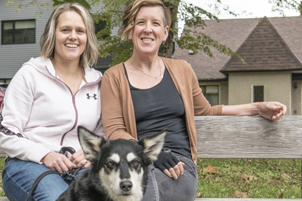 Lesbian couple with their dog seated on a bench.