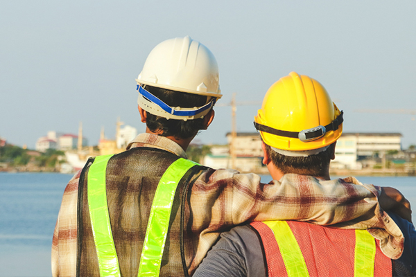 Two dock workers looking out at the river, one with his arm around his friend.