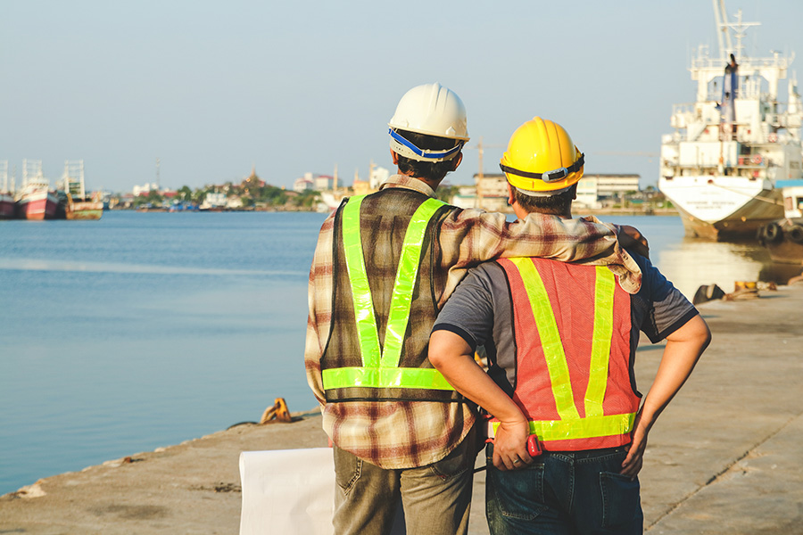 Two dock workers looking out at the river, one with his arm around his friend.