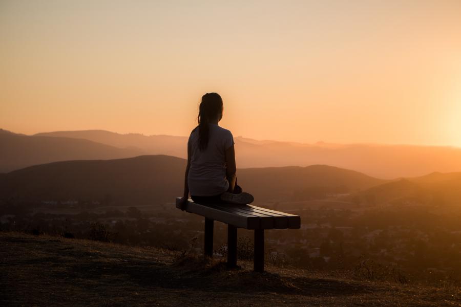 Woman sitting on bench at sunset